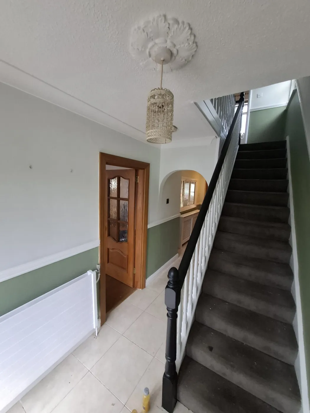 Hallway with ceiling rose and dado rail repainted in sage green and white, with a black handrail and newel post, by Original Dublin Painter